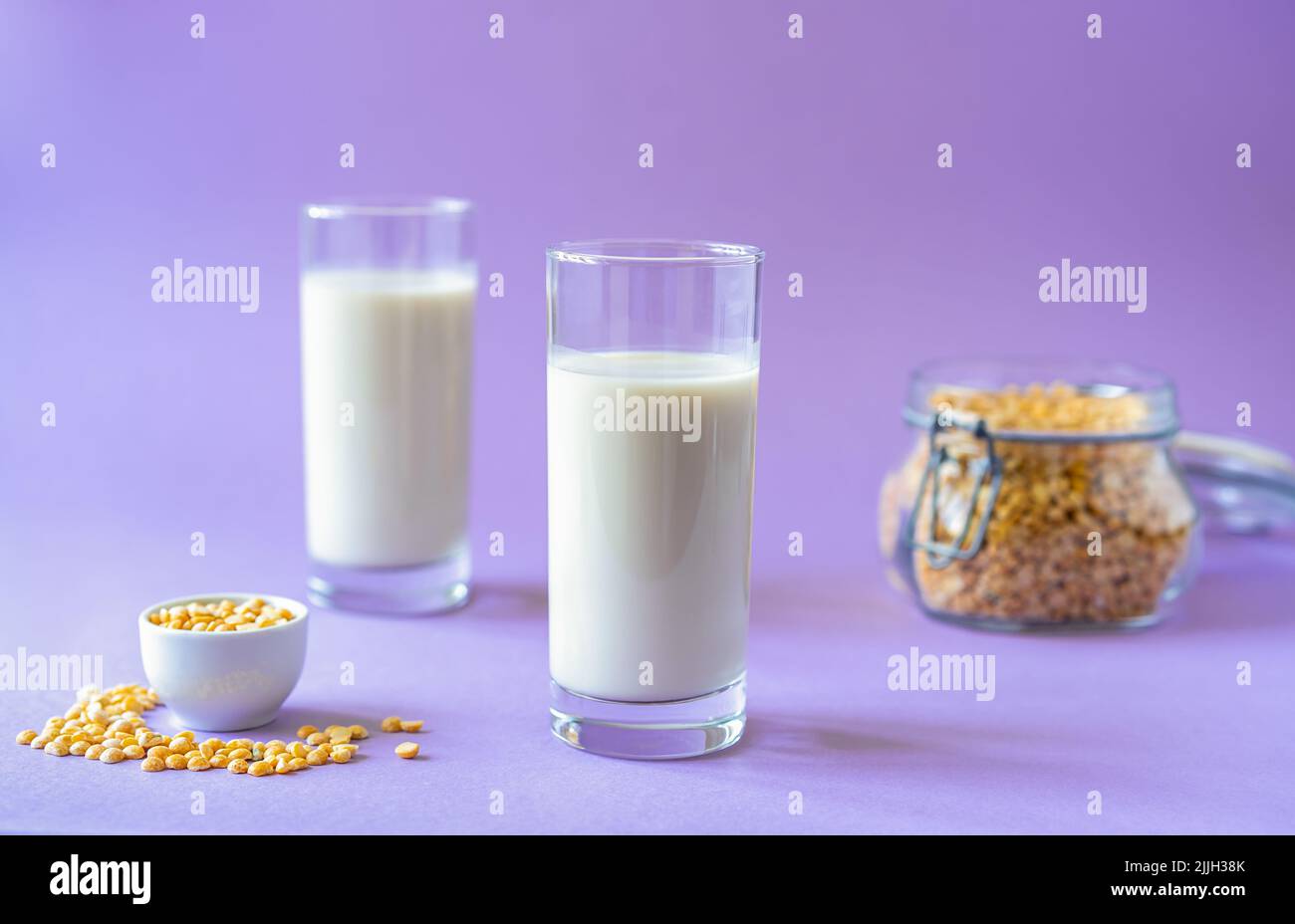 Vegan healthy pea milk in two glasses, pea seeds. Lilac background. Copy space Stock Photo