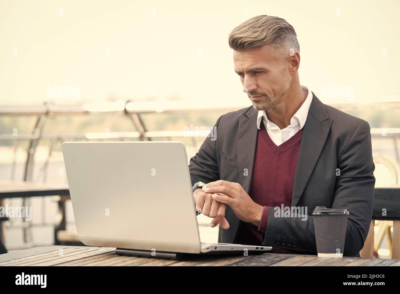 Serious professional man check time on watch working on laptop computer ...