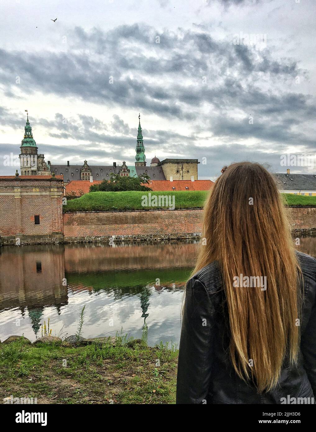 A vertical shot of a girl looking towards the Kronborg castle under a cloudy sky Stock Photo