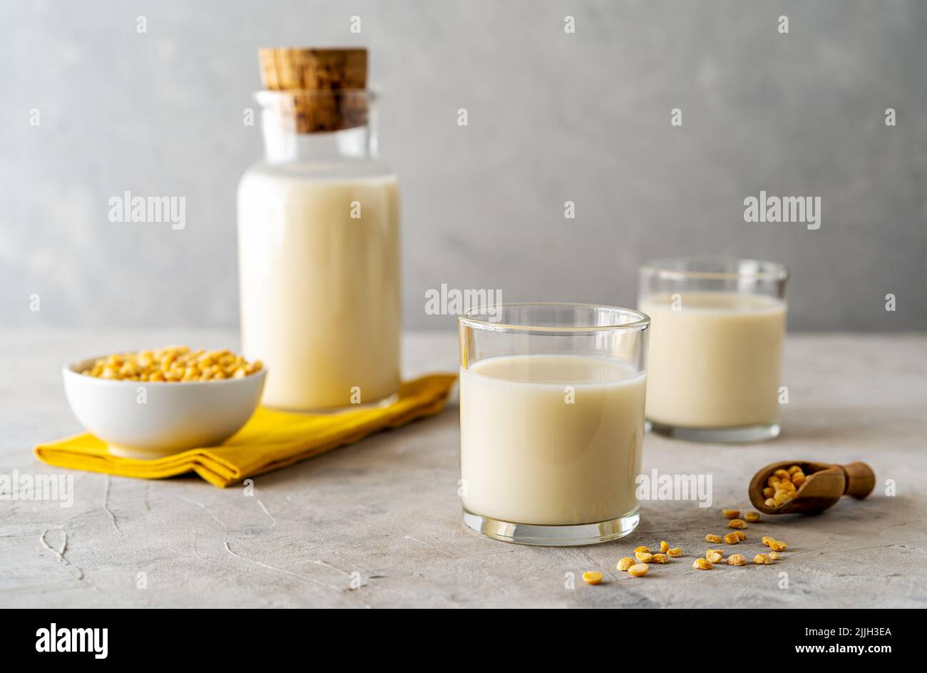 Vegan healthy pea milk in glass bottle and two glasses, concrete background, pea grains, yellow napkin. Copy space Stock Photo