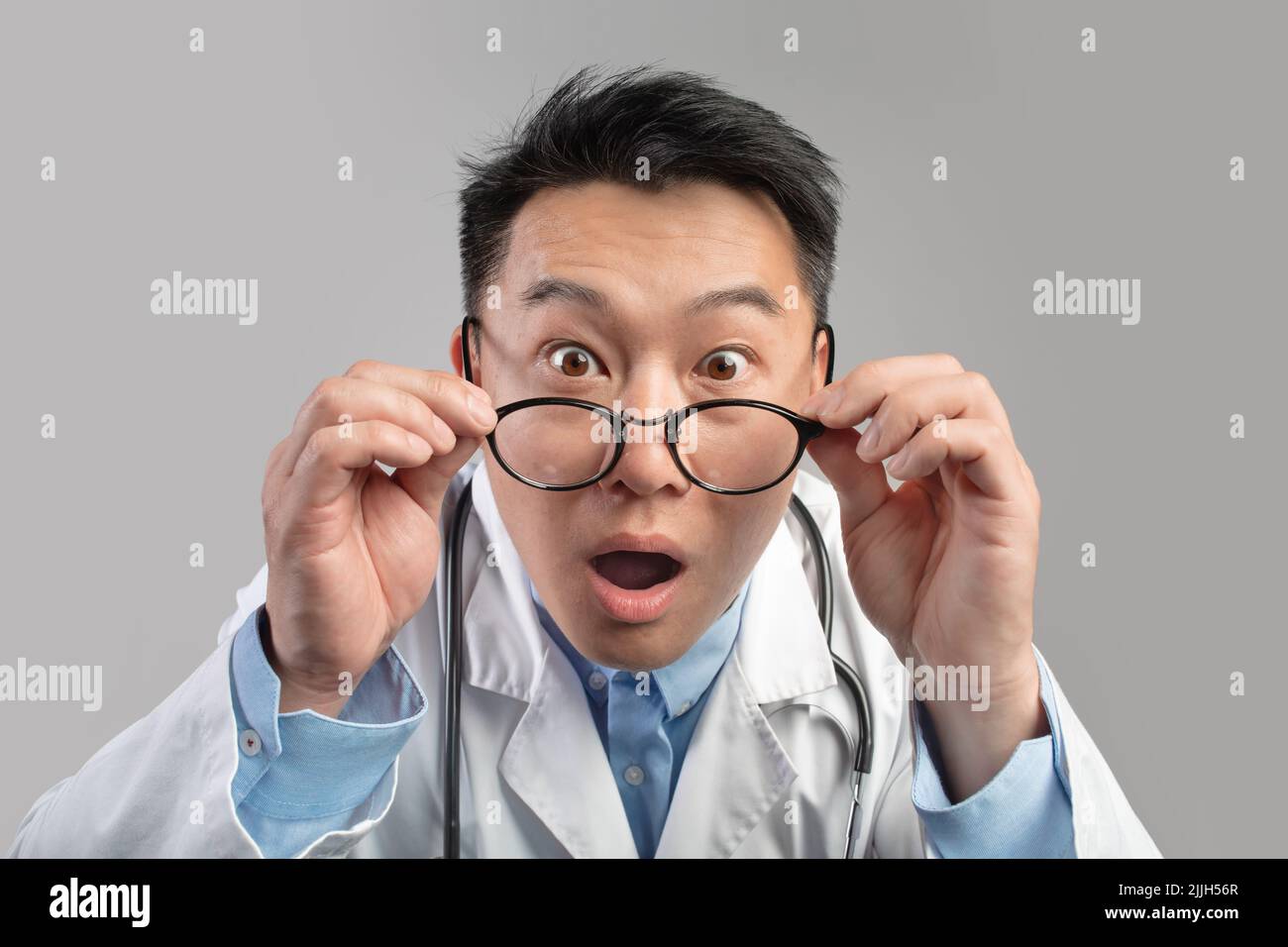 Portrait of shocked excited funny adult asian man doctor in white coat with open mouth, takes off glasses Stock Photo