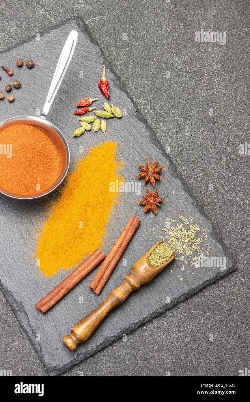 Dry spices in wooden scoop. Ground turmeric in metal bowl and paprika on table. Cinnamon sticks, star anise and cardamom. Copy space. Flat lay. Black Stock Photo
