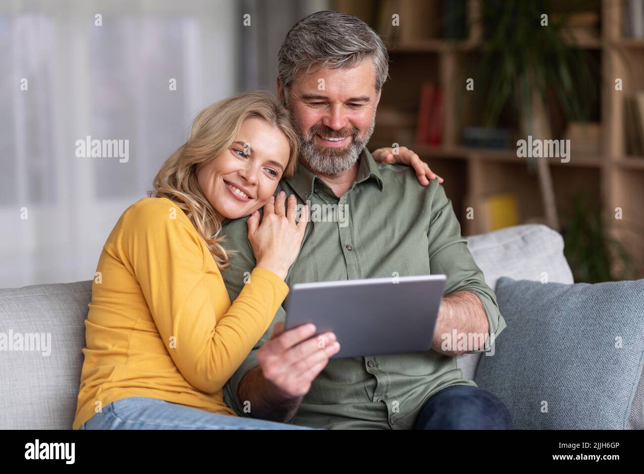 Great App. Happy Middle Aged Spouses Using Digital Tablet Together At Home Stock Photo