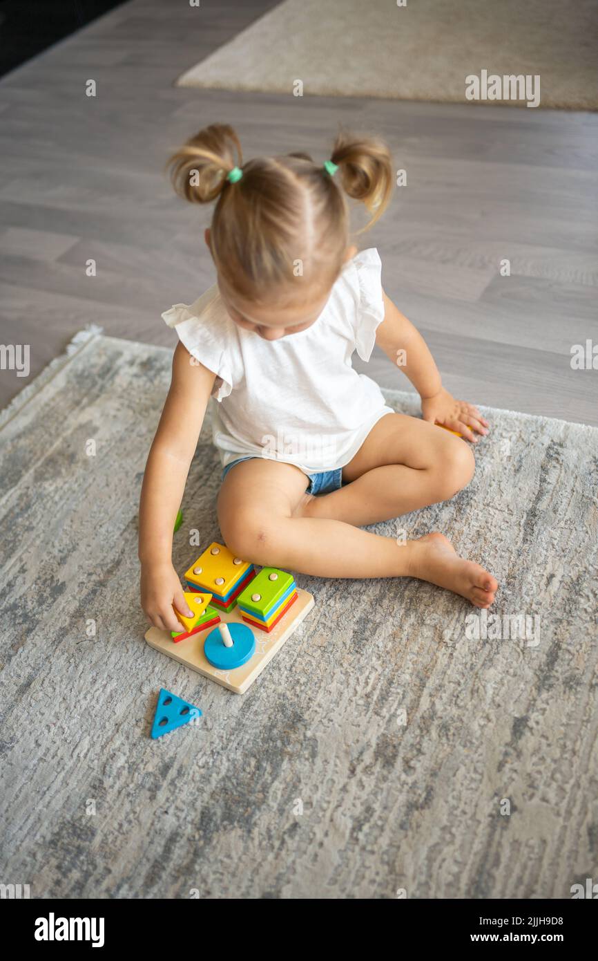 Cute caucasian little girl playing on the floor at home with eco wooden