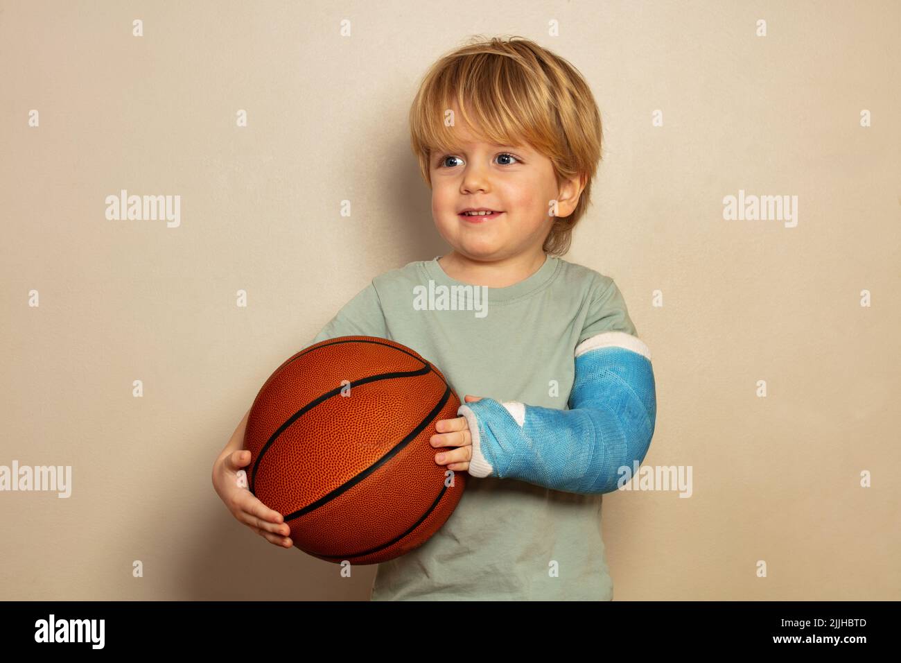 Boy hold basketball ball with broken hand in plaster cast Stock Photo