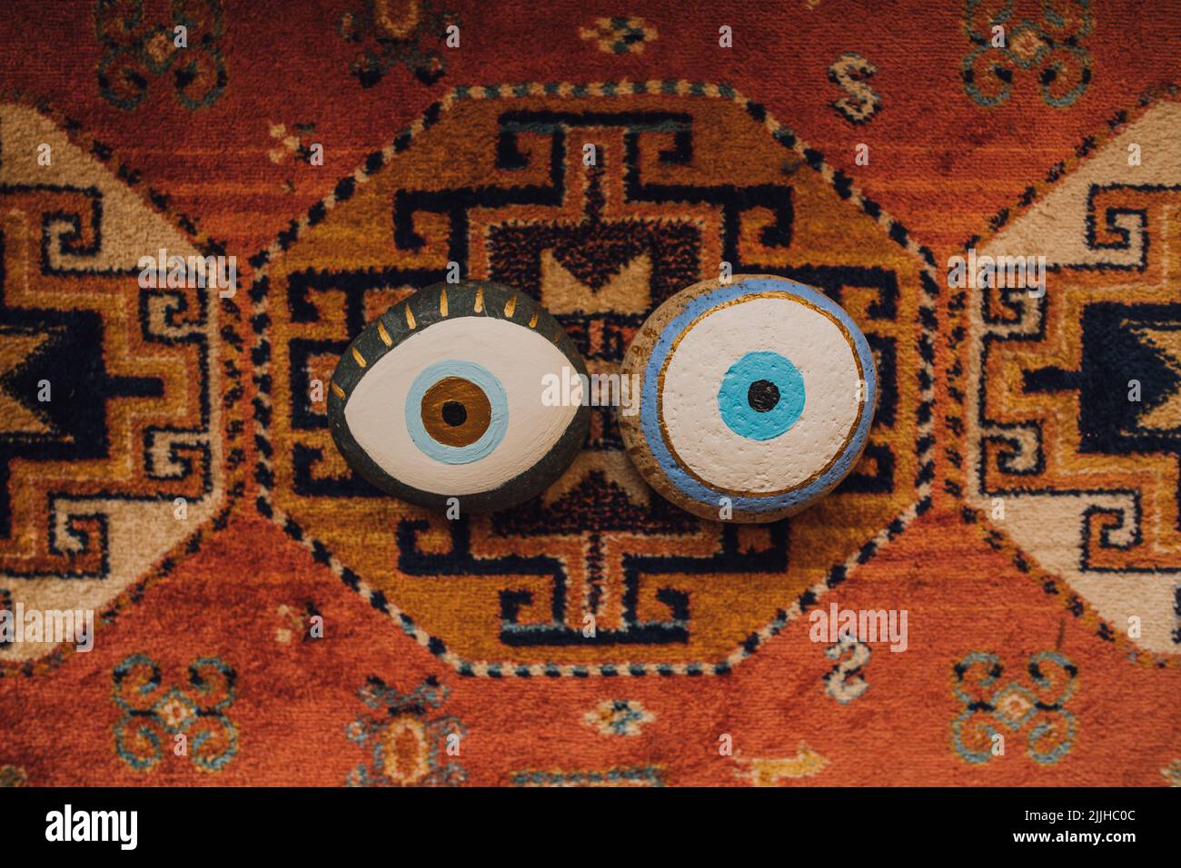 two painted evil eye rocks on patterned rug Stock Photo