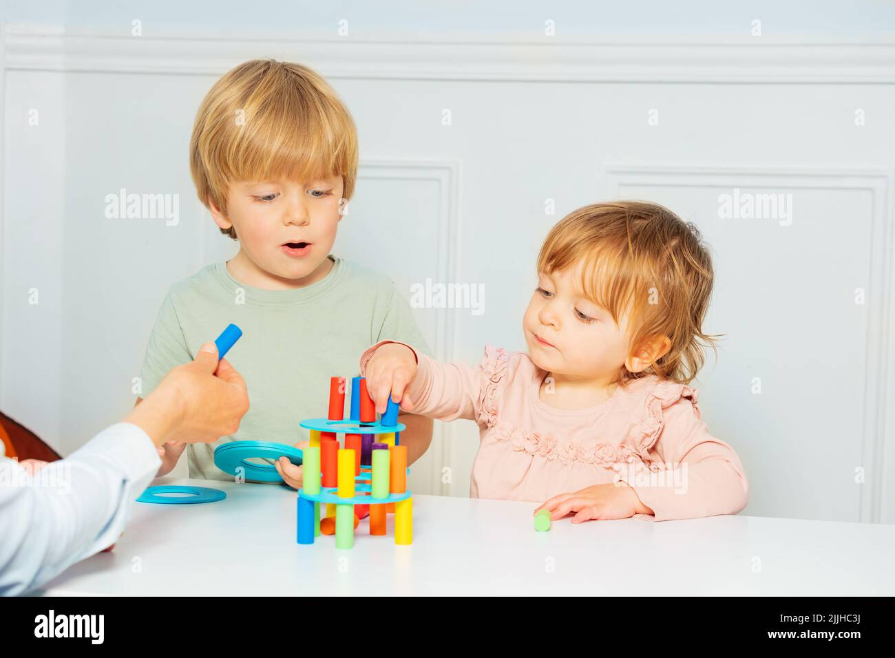 Cute boy and girl build with help of adult tower on the table Stock Photo
