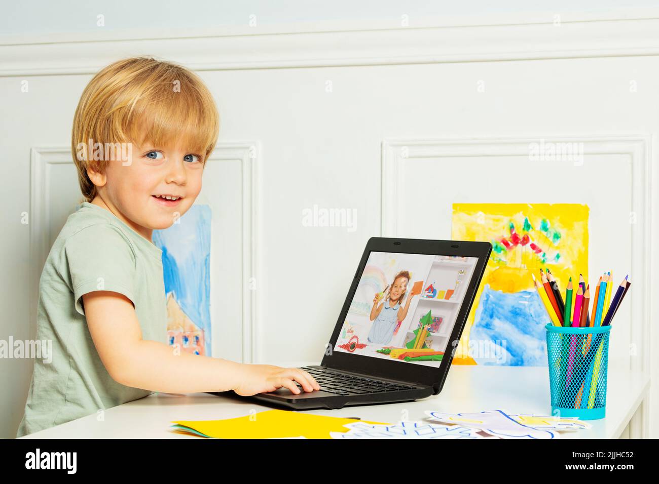 Cute smiling blond boy in headphones using laptop for education Stock Photo
