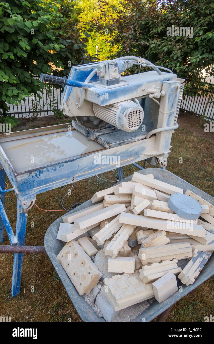 Next to a circular saw for stones there is a wheelbarrow with stone