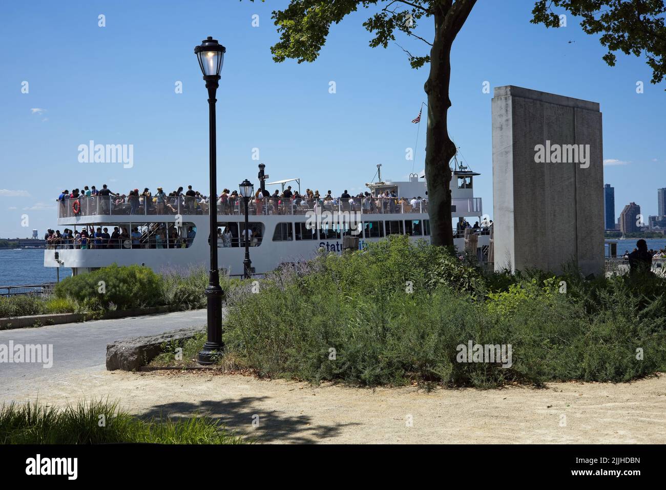 New York, NY, USA - July 25, 2022: View from Battery Park grounds towards the Hudson River with War Memorial in foreground and docking tourist boat in Stock Photo