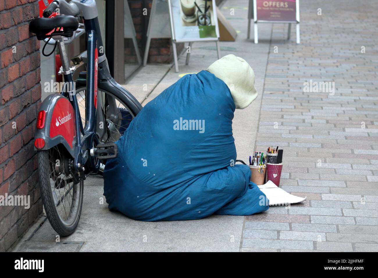 London, UK - Nov 21, 2021: homeless poor man painting while sitting on a pavement. Stock Photo