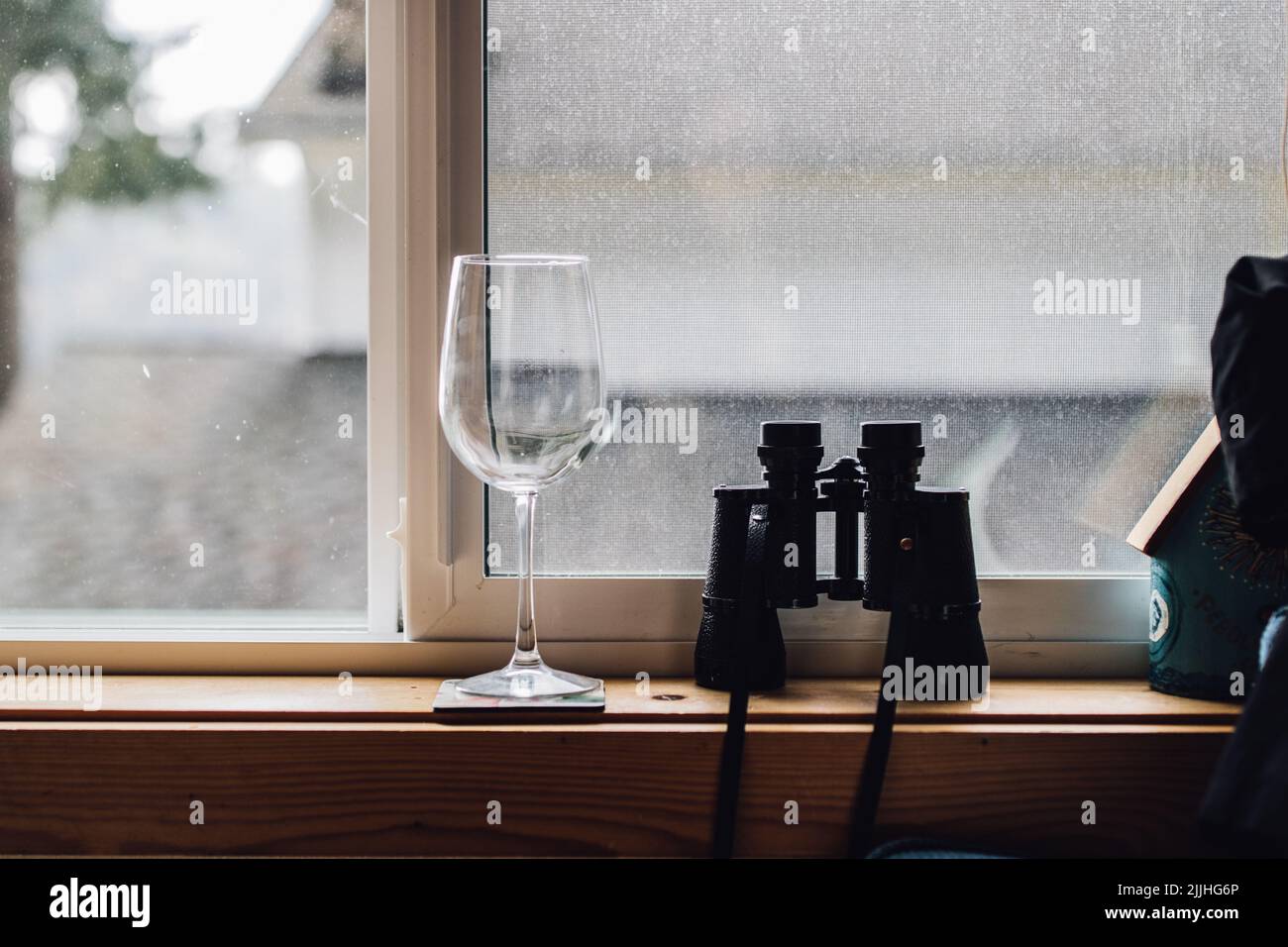 binoculars and wine glass sitting on window sill. neighborhood watch concept Stock Photo