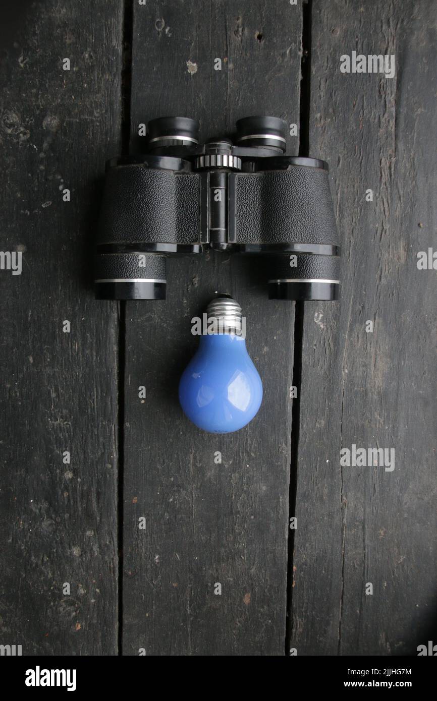 Creative background with binoculars and blue light bulb Stock Photo
