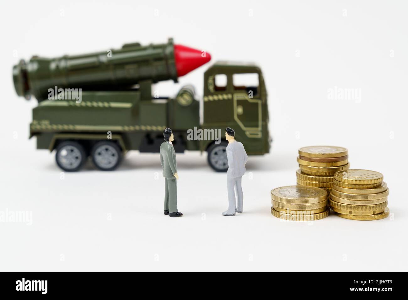 The concept of the military budget. On a white surface are figurines of people, coins and a toy military vehicle. Stock Photo