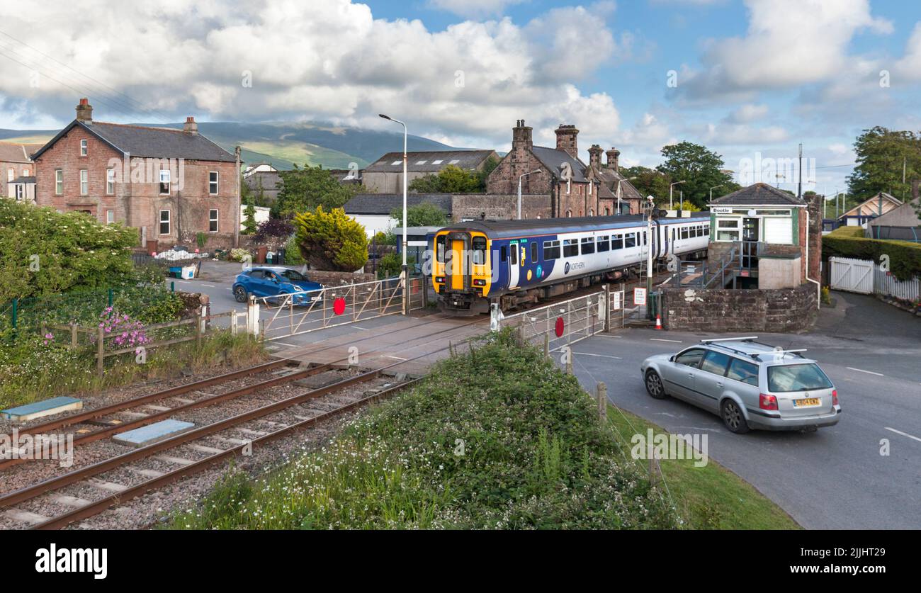 Northern Rail class 156 train at the village railway station at Bootle, Cumbria with manual level crossing gates and the mechanical signal box Stock Photo