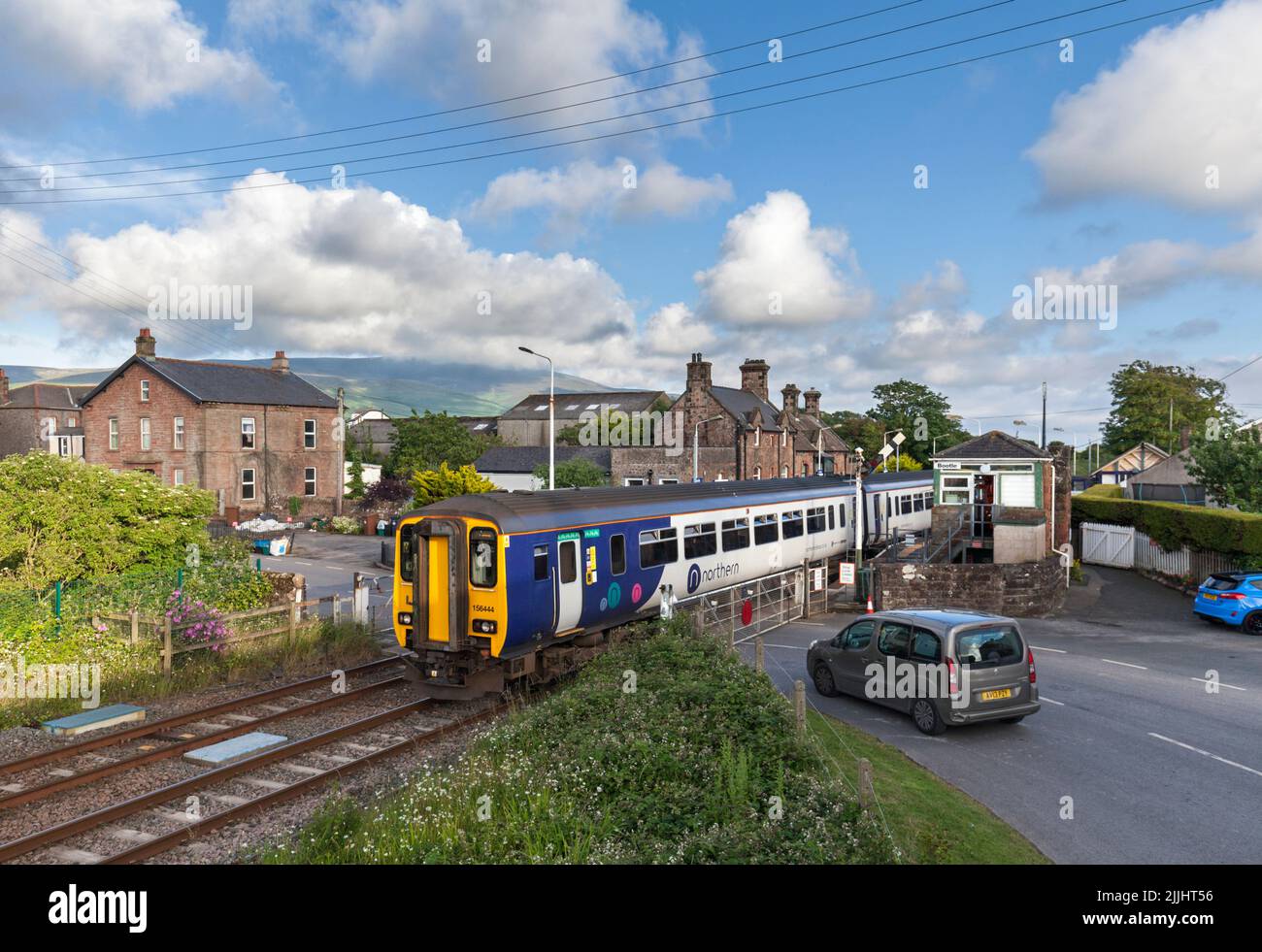 Northern Rail class 156 train at the village railway station at Bootle, Cumbria with manual level crossing gates and the mechanical signal box Stock Photo
