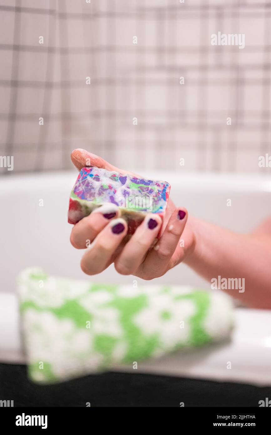 A masculine hand with painted nails holds a bar of soap with psychedelic swirls. A green floral