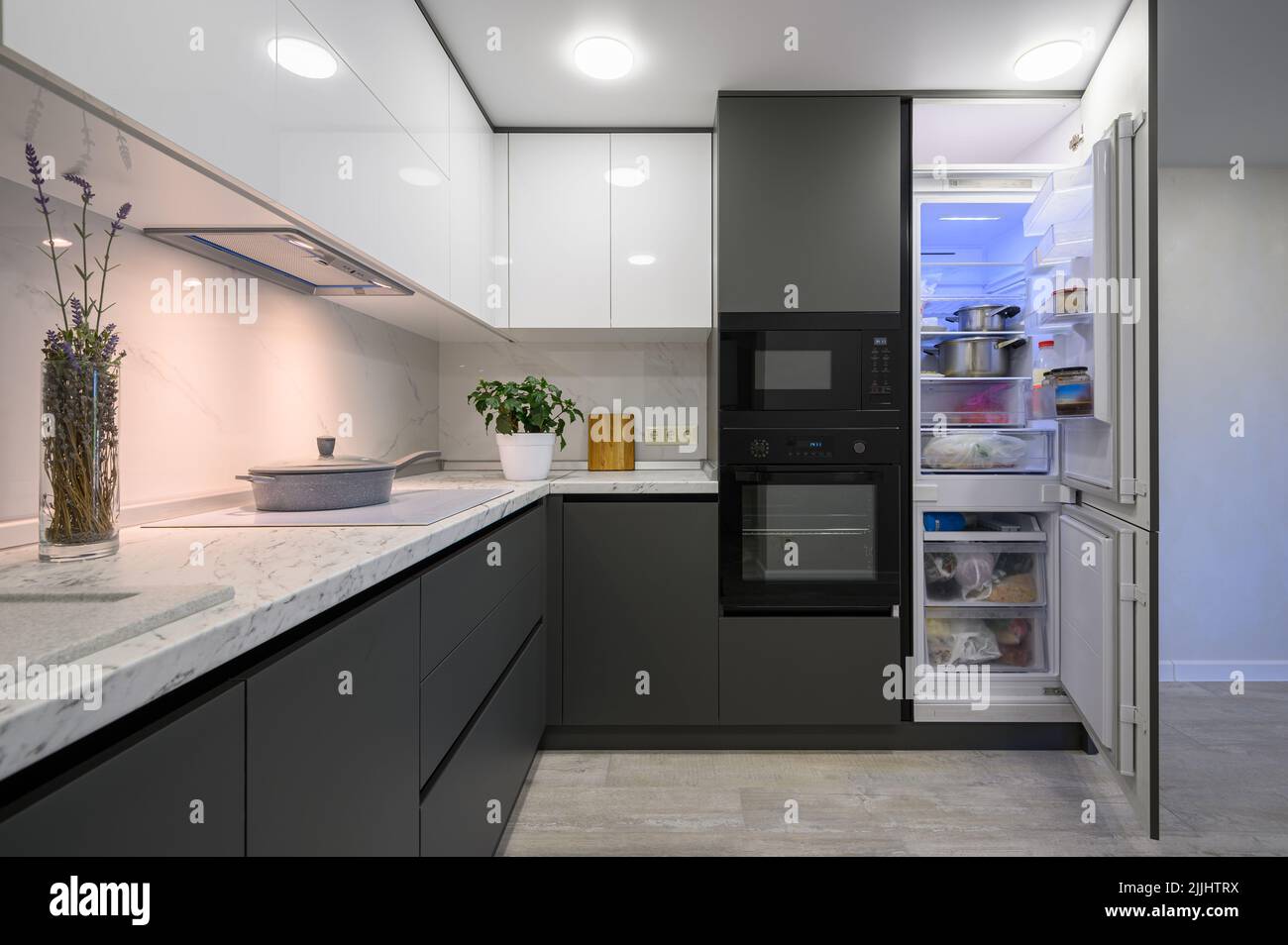 Modern simple trendy dark grey and white kitchen with fridge open Stock Photo