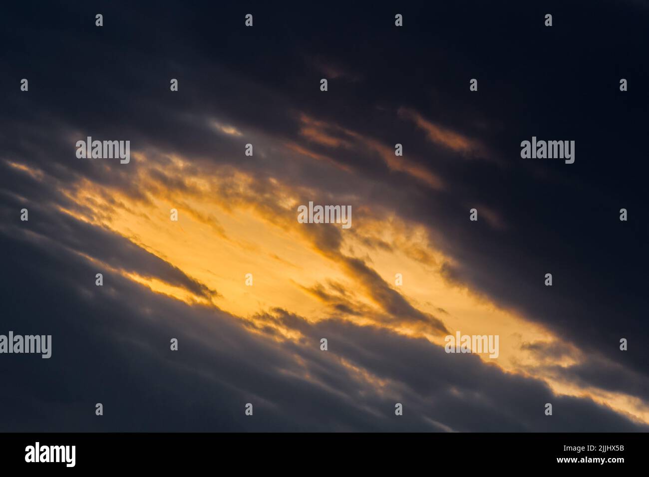 Light spot orange sunset through dark rain clouds storm beam light sky weather background. Stock Photo