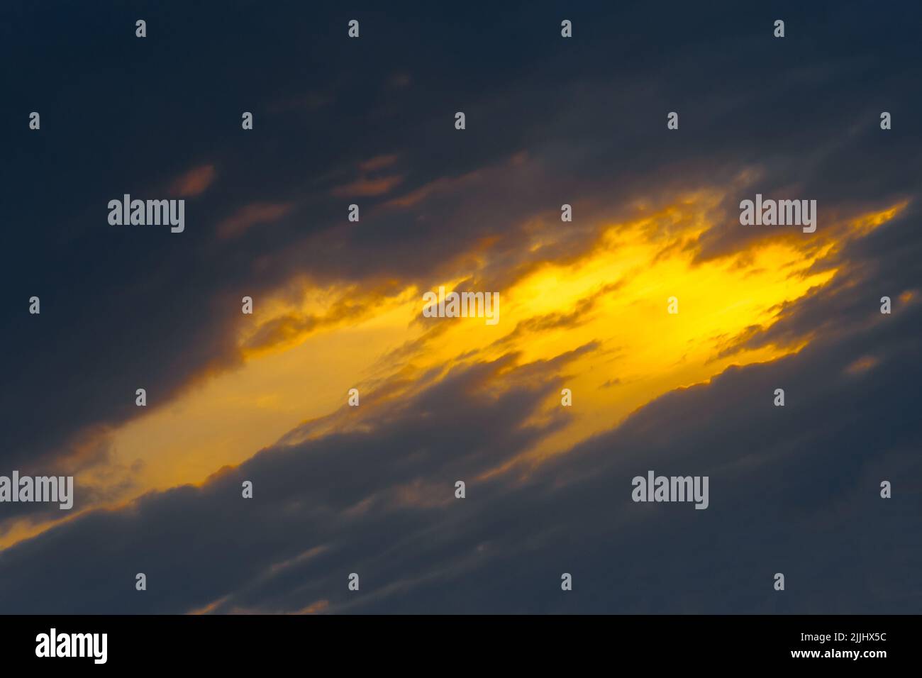 Light spot orange sunset through dark rain clouds storm beam light sky weather background. Stock Photo