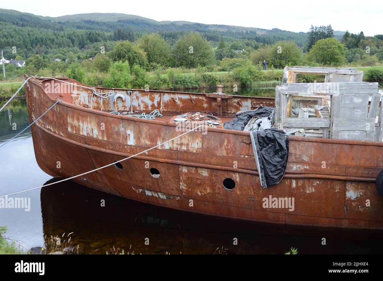 A boat that has seen better days on the Caledonian canal, Fort Augustus,, the rusting decay contrasting with the vibrancy of the surounding countrysid Stock Photo