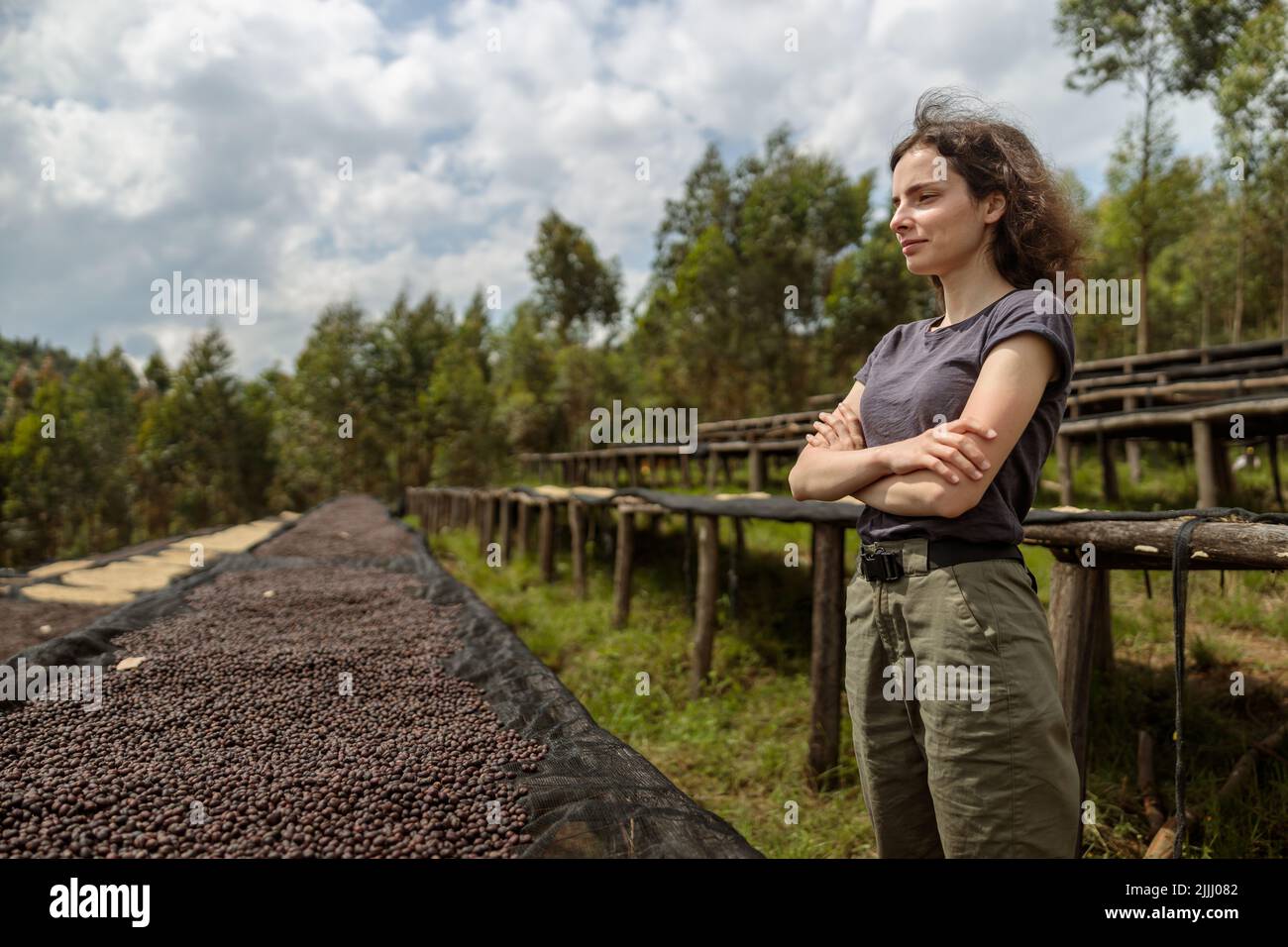 Pretty lady with arms crossed standing near tables of drying coffee beans Stock Photo