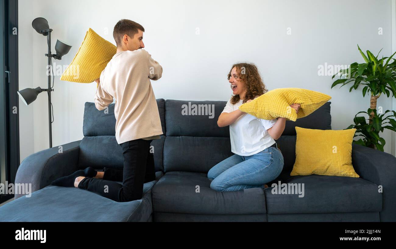 Couple of two happy boyfriends having fun playing together on the sofa at home fighting with cushion enjoying. Pillows war indoors at the morning Stock Photo