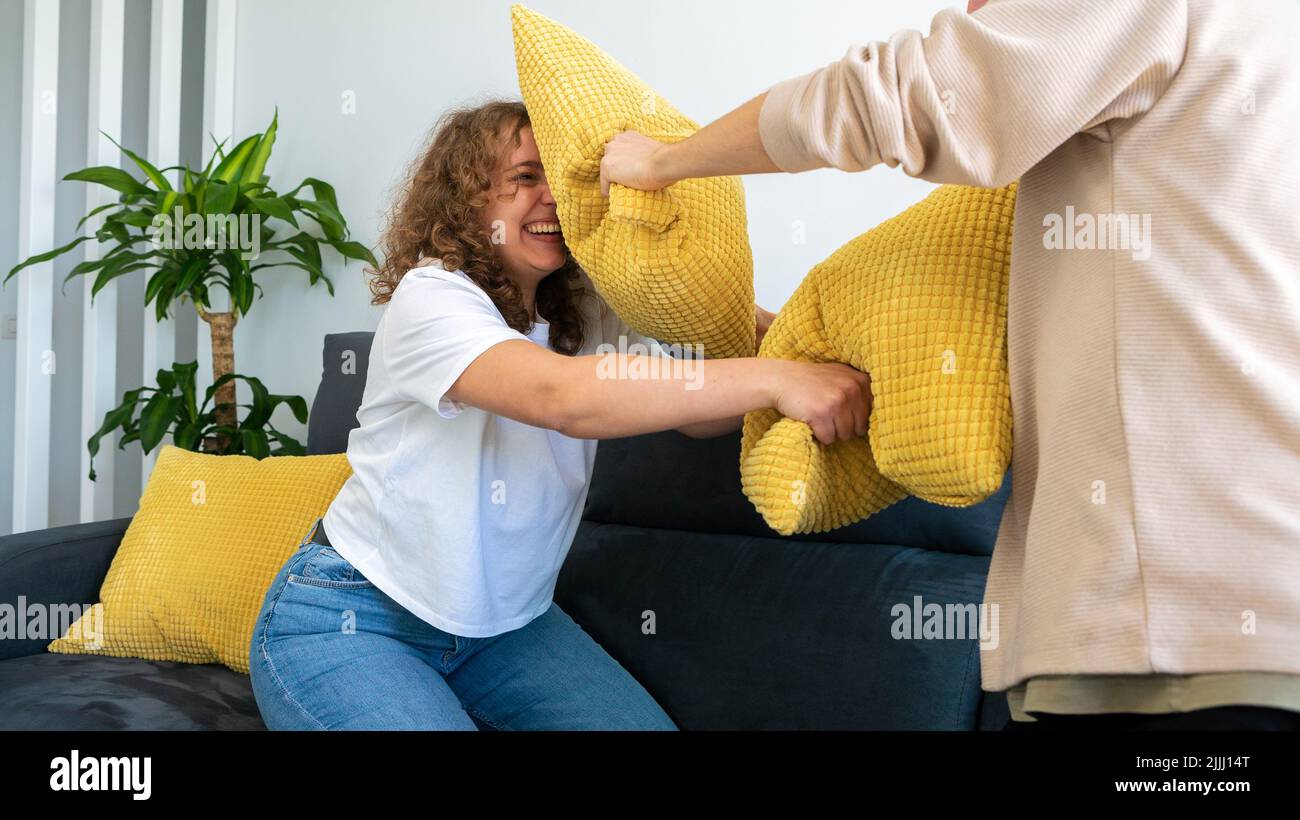 Boyfriends couple doing pillow battle during morning time at home. Happy young people enjoying time together. Joyful millennial lifestyle and funny re Stock Photo