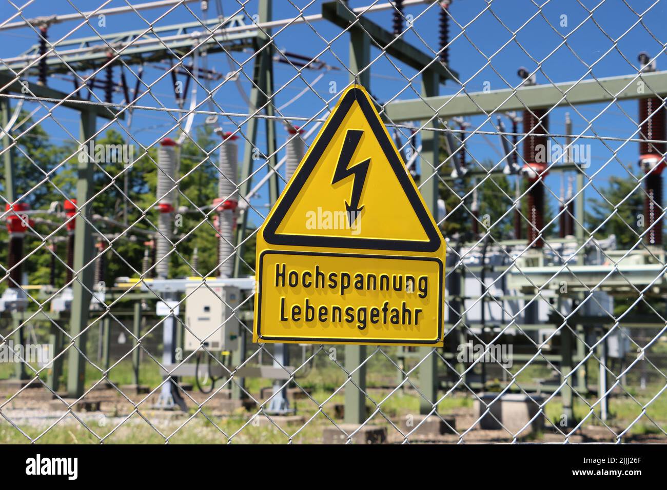 Attention: high voltage, danger for life is translation for german 'Hochspannung Lebensgefahr'. at transformer station during summertime with blue sky Stock Photo