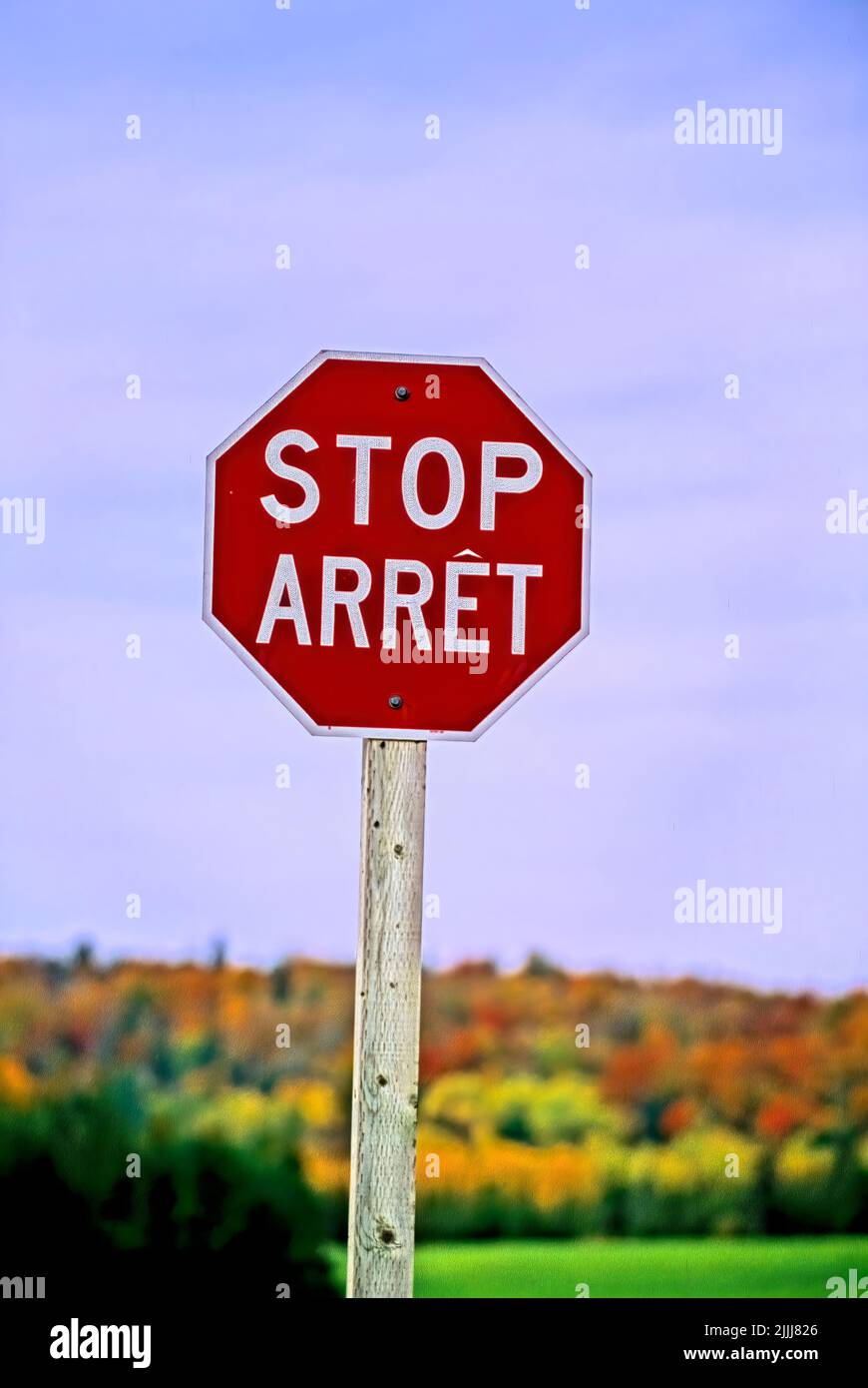 A vertical  image of a red bilingual stop sign located in rural New Brunswick Canada Stock Photo