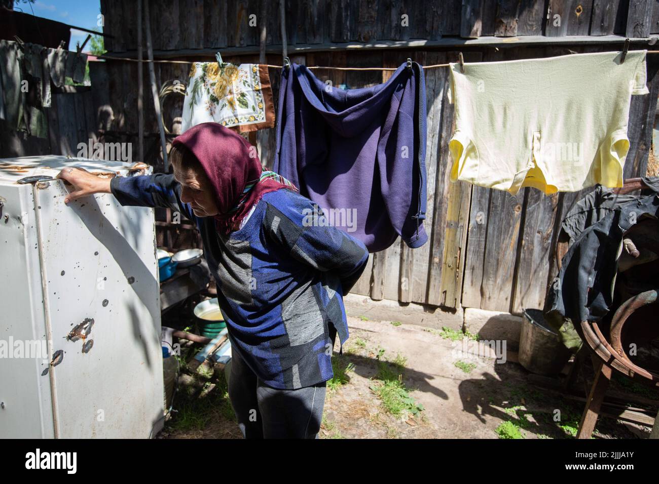 Makariv, Ukraine. 23rd July, 2022. A woman leans on an old refrigerator destroyed by fragments of artillery shells. Drying laundry in a rural yard hangs in the background. Russia invaded to Ukraine on February 24, 2022. (Credit Image: © Oleksii Chumachenko/SOPA Images via ZUMA Press Wire) Stock Photo