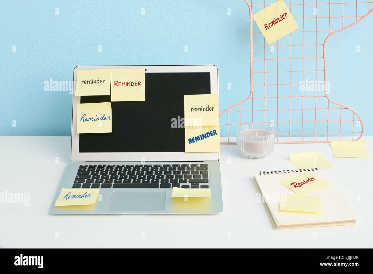 Laptop with sticky notes on table near blue wall Stock Photo