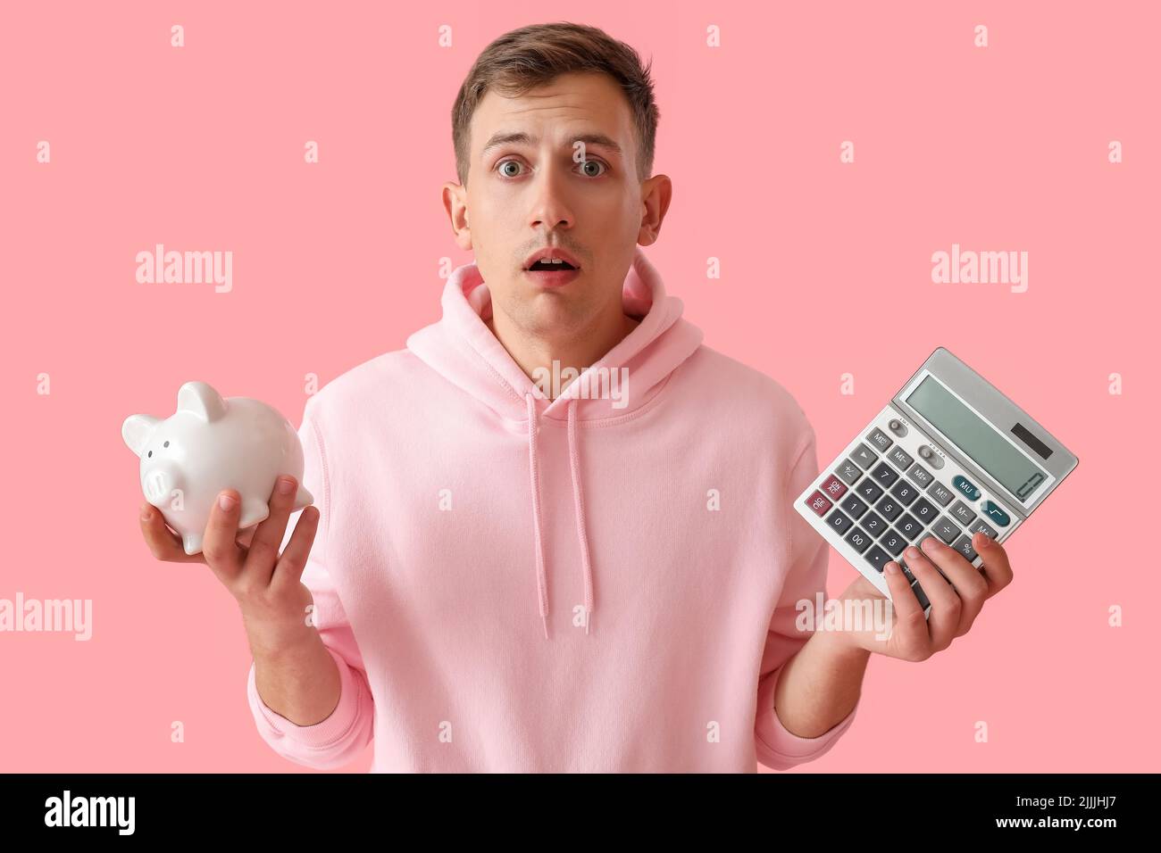 Shocked young man with piggy bank and calculator on pink background ...