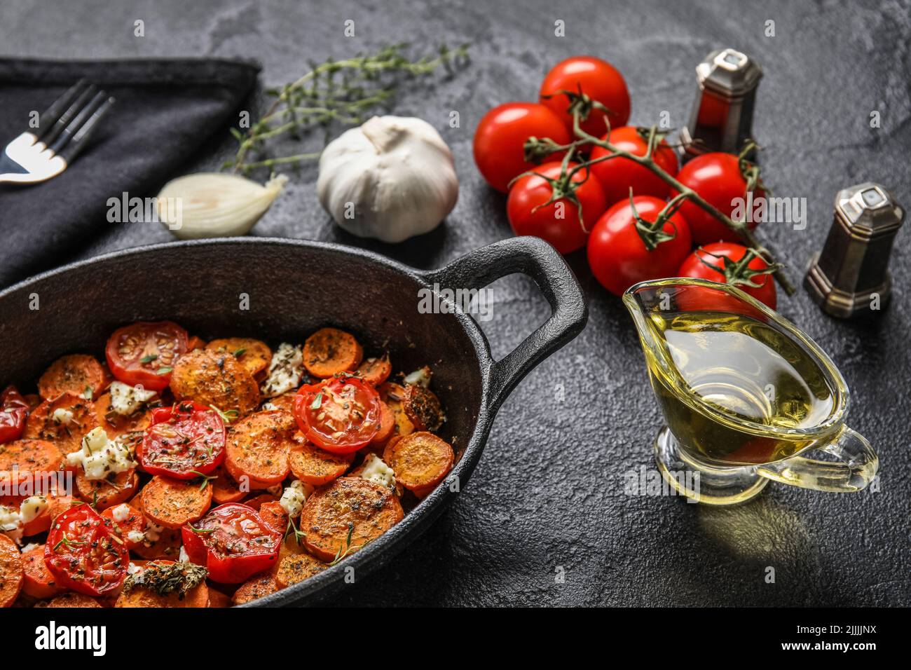 Frying pan with baked vegetables and gravy boat of oil on dark ...