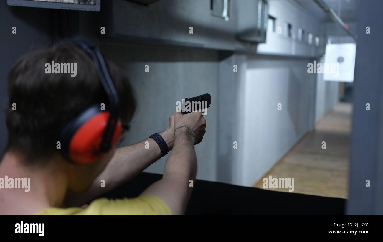 Man shooter in tactical headphones aiming pistol at target in shooting