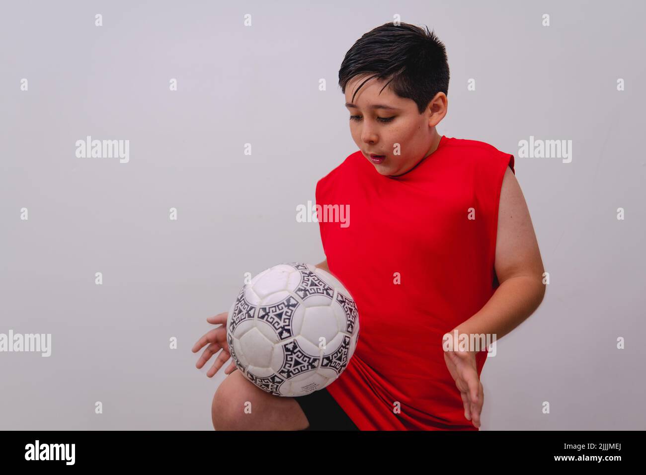 Boy dressed in sportswear doing a pullup with a soccer ball. Boy with