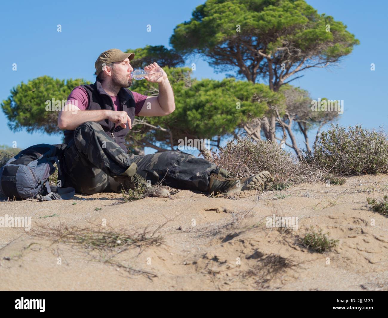 Tourist man drinking water from the plastic bottle during break in a desert walk. Travel concept. Stock Photo