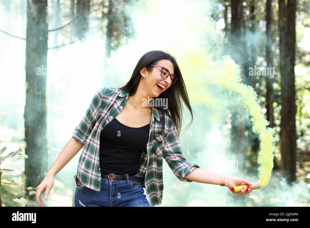 Young woman in a photoshoot holding a smoke bomb yellow in the forest smiling at Costa Rica Stock Photo