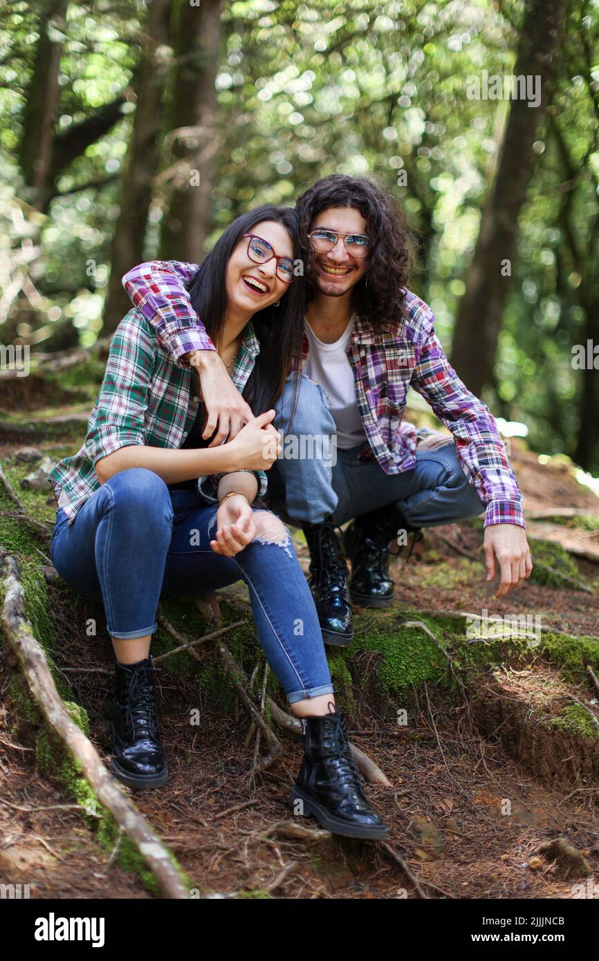 Young latin couple sitting in the forest smiling looking camera with his hand over her shoulder at Costa Rica Stock Photo