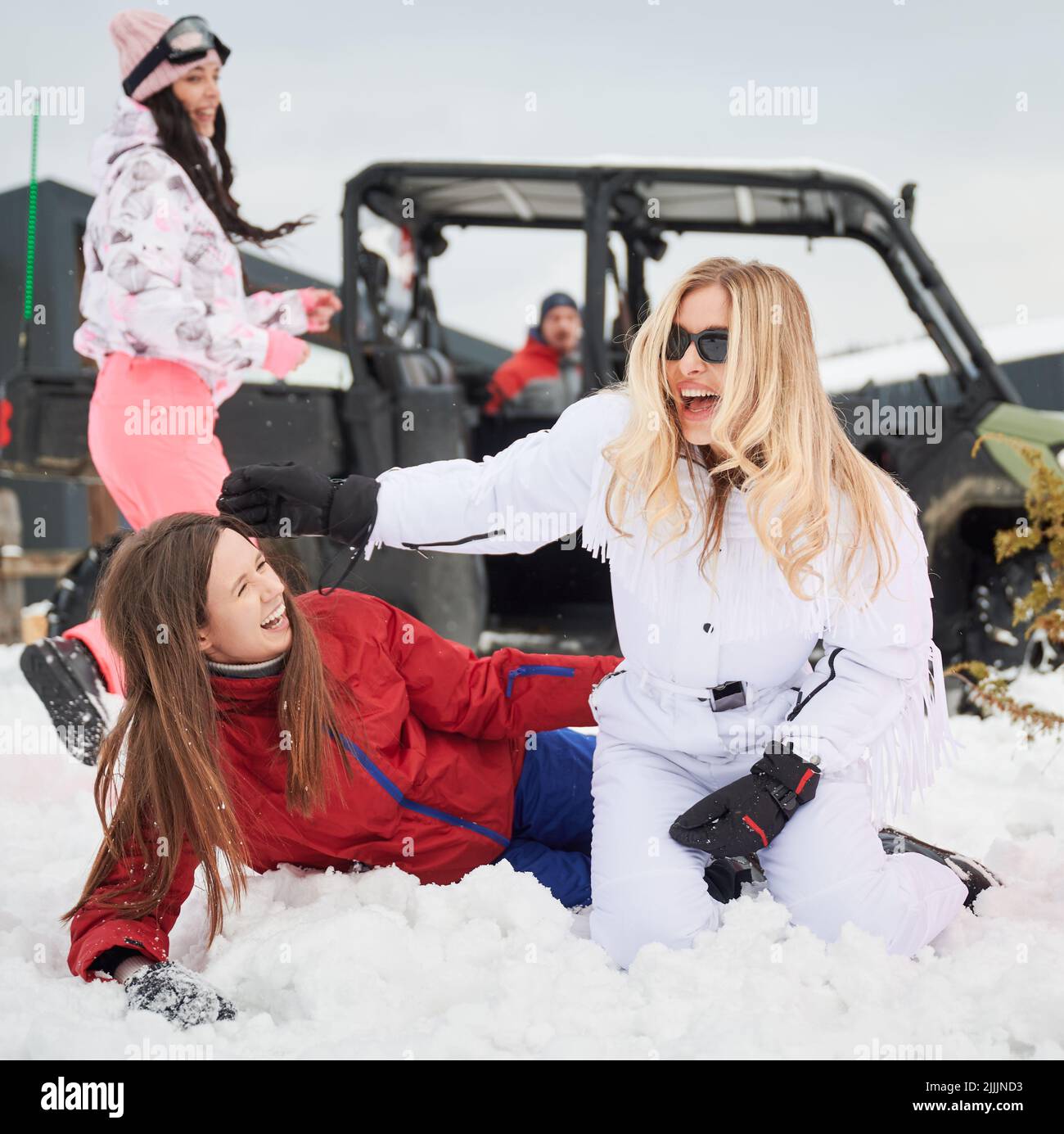 Happy women having fun in snow. Off-road buggy car on background. Concept of active leisure and winter activities. Stock Photo