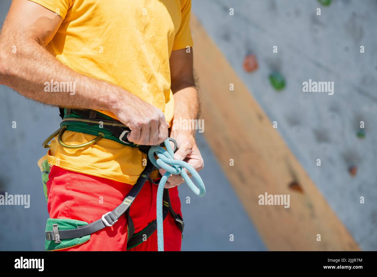 A climber knits a knot. A man prepares to climb a climbing route