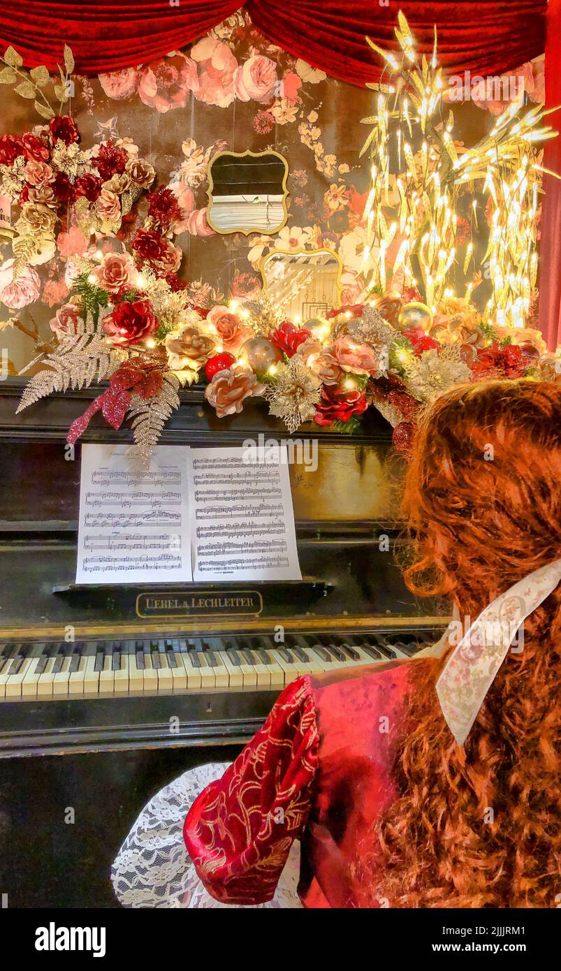 Portrait of a beautiful redhead young woman at Christmas by candlelight, who put her hands on the keys of an old brown buffet piano. The concept of the holiday, people, beauty, New Year, Christmas. High quality photo Stock Photo
