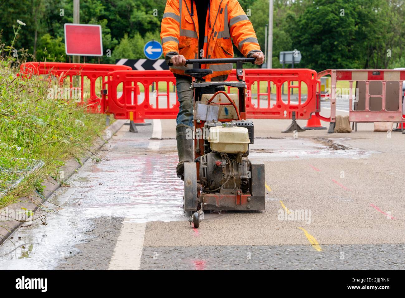 Builder using petrol powered road saw with dimond blade to cut asphalte road surface Stock Photo
