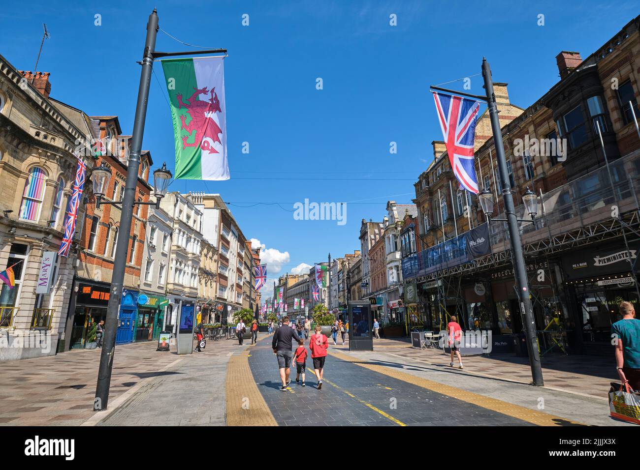People walking pedestrian St Mary street, flags flying for the Queen's jubilee on a sunny day. In Cardiff, Wales, United Kingdom. Stock Photo