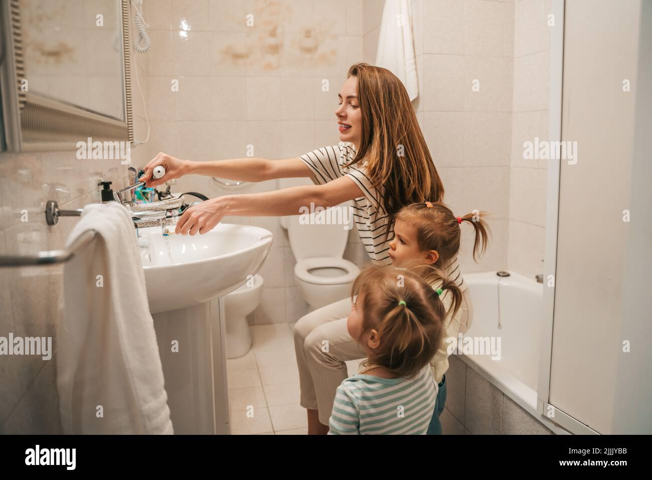Cheerful young mother teaching her children how to brush teeth Stock Photo