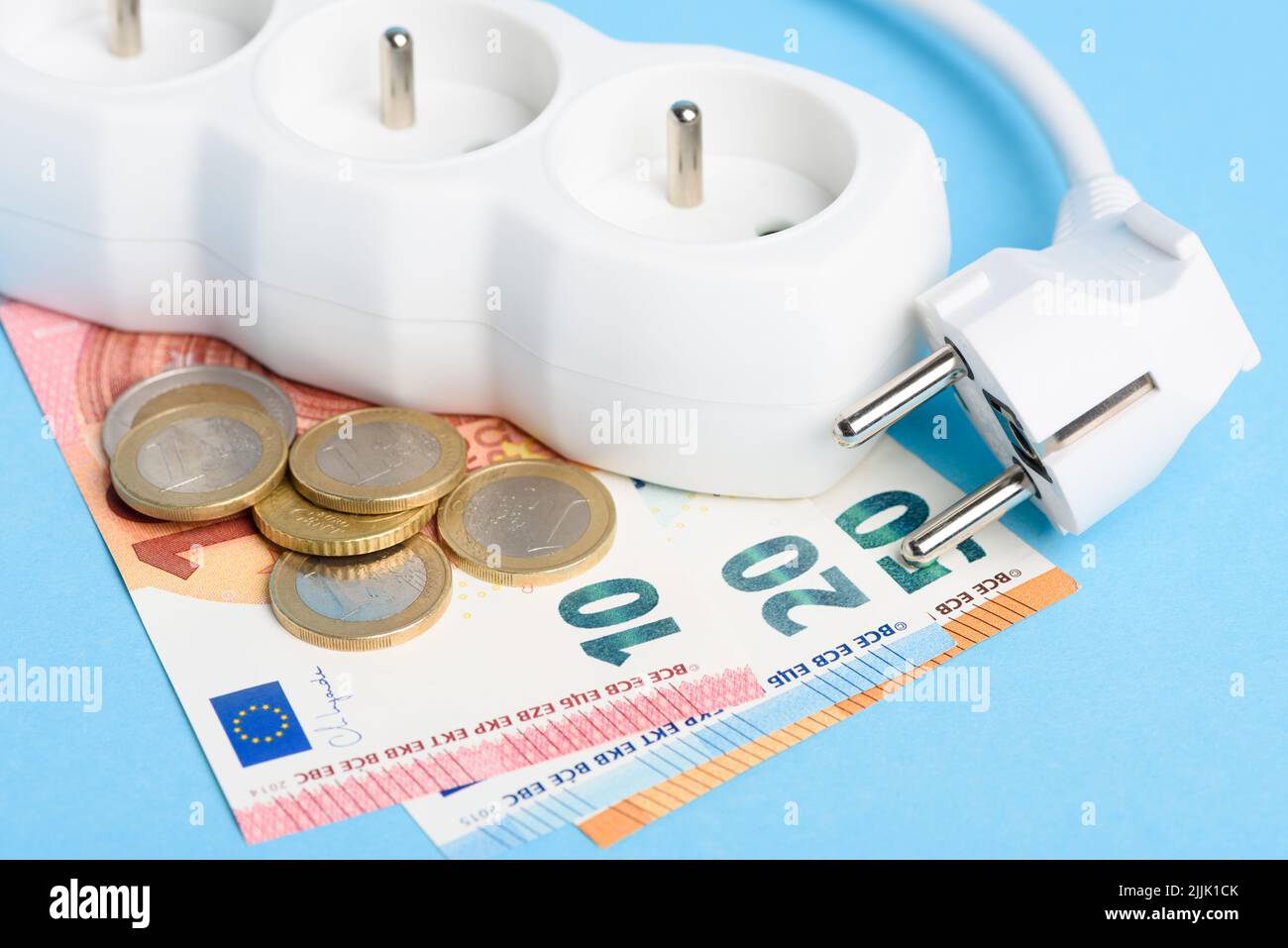 Euro bills and coins with power strip and plug on blue background. Concept of expensive electricity costs in Europe and rise in energy bill prices Stock Photo