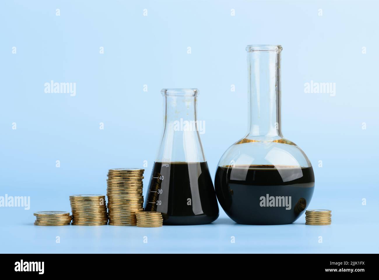 Crude oil in glass beakers with coins stacks on blue background, fuel price concept Stock Photo