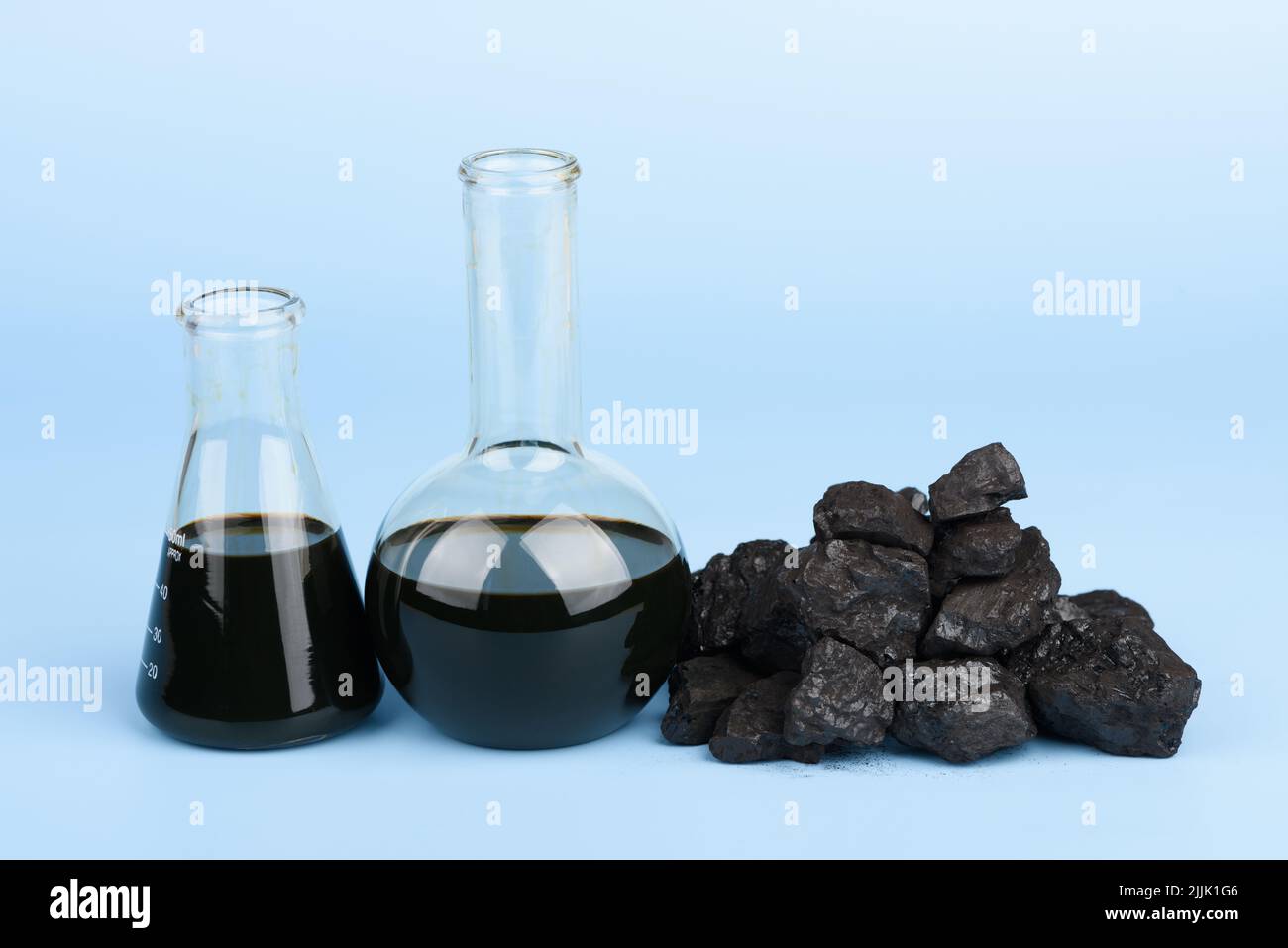 Crude oil in glass beakers and black hard coal lumps on blue background, fossil fuel concept Stock Photo