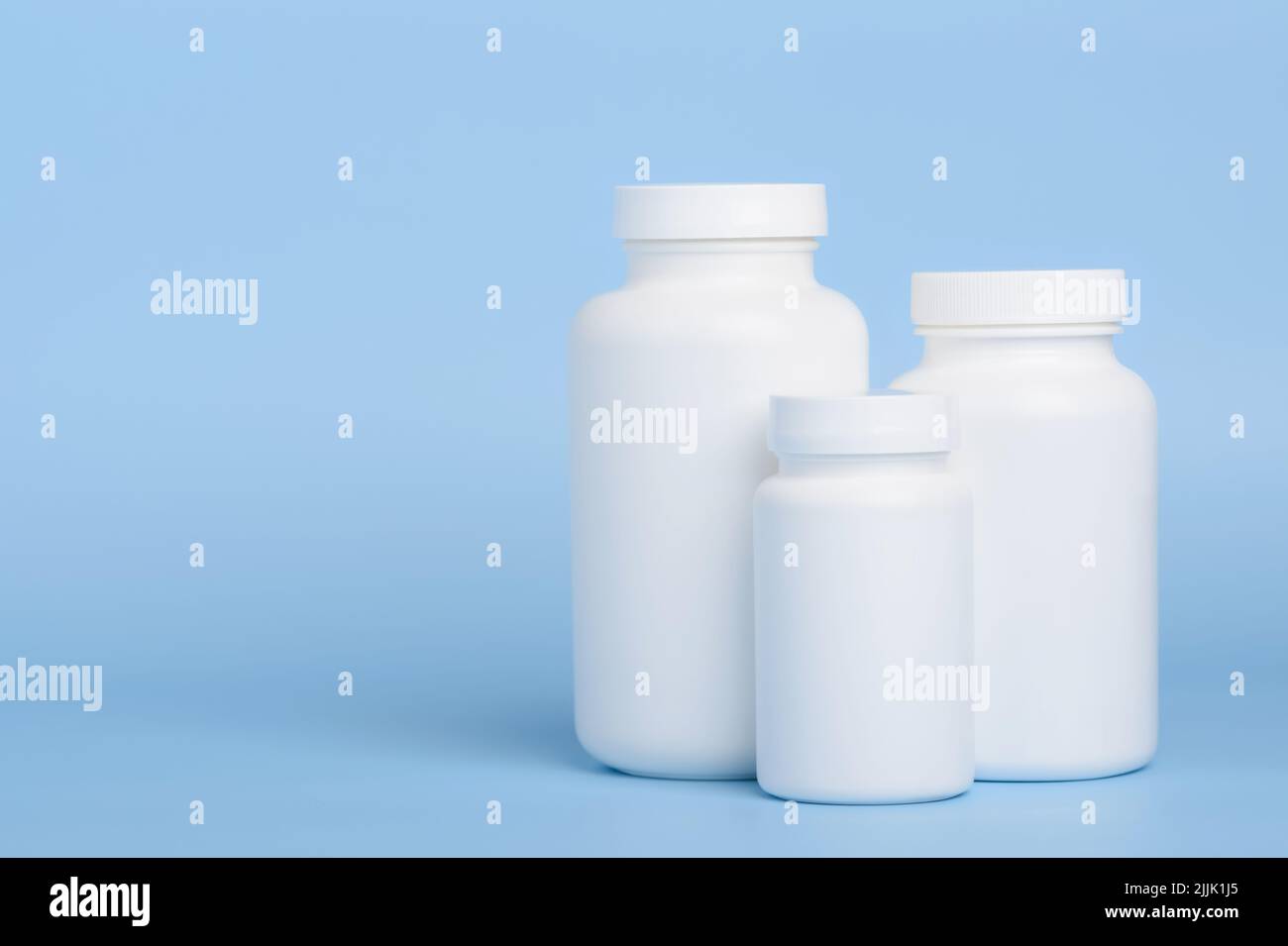 Three blank white plastic bottles of medicine pills or supplements on blue background with side copy-space Stock Photo