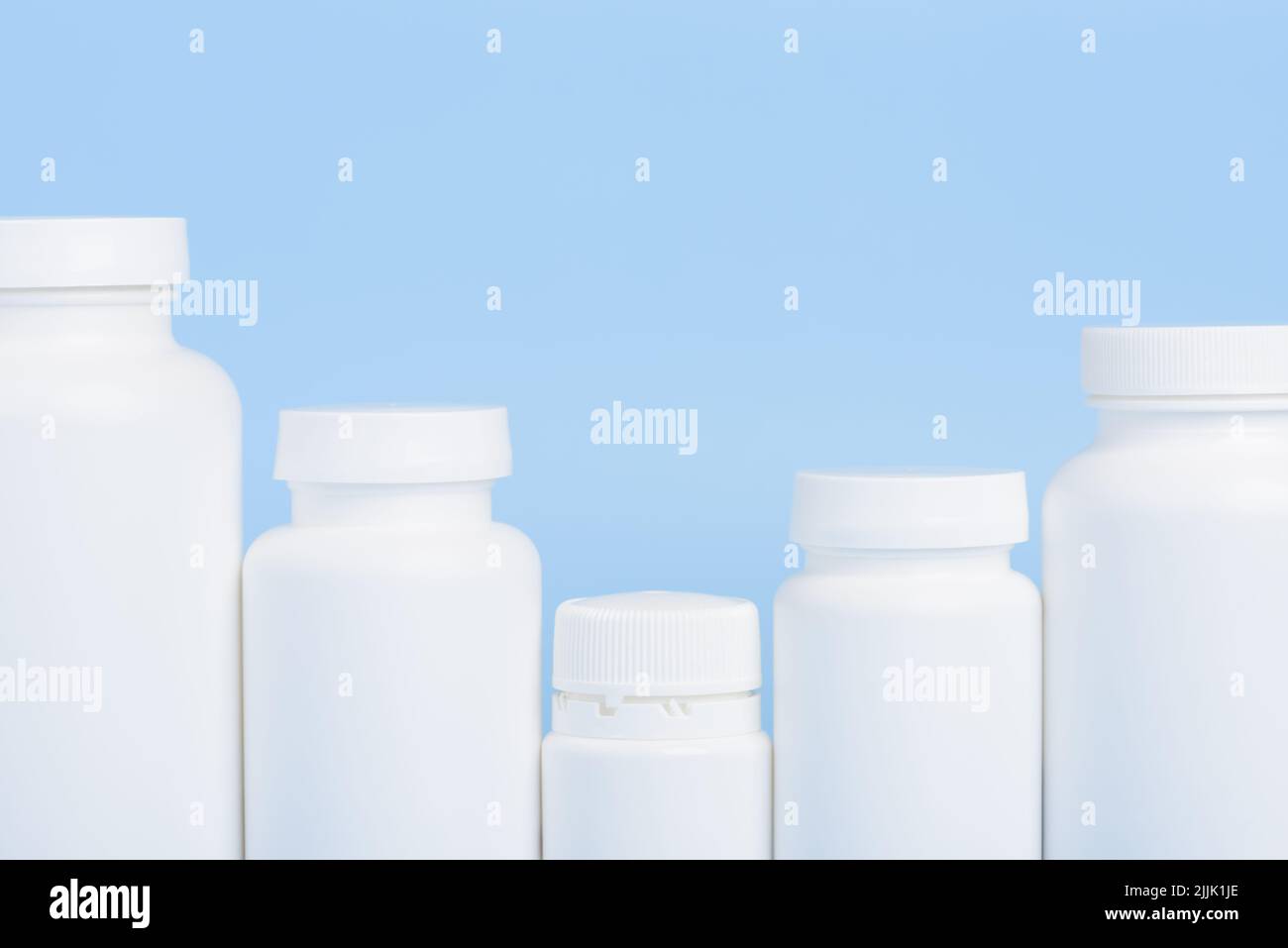 Row of blank white plastic bottles of medicine pills or supplements on blue background Stock Photo